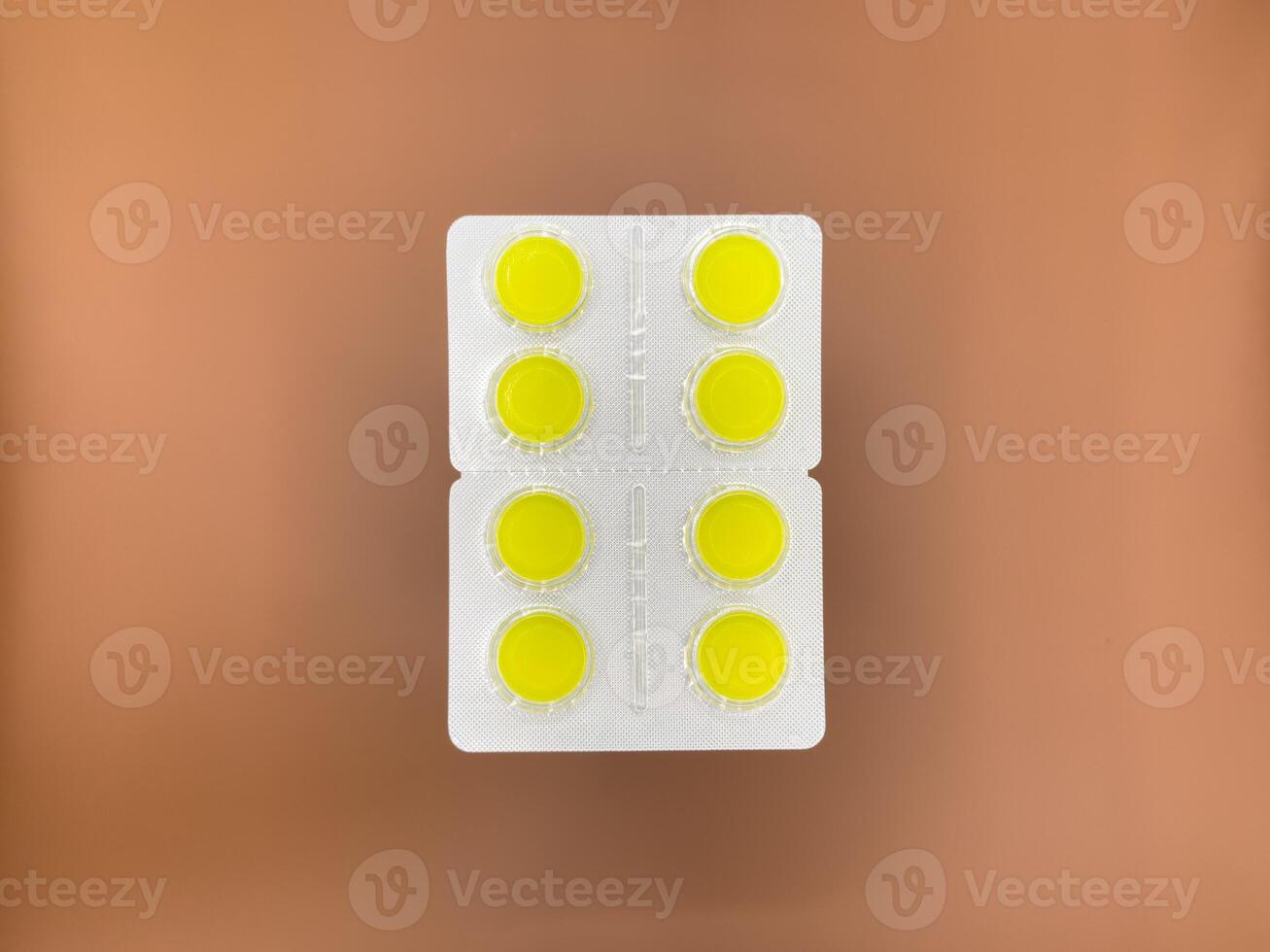Yellow cough tablets in silver packaging on beige background, top view photo