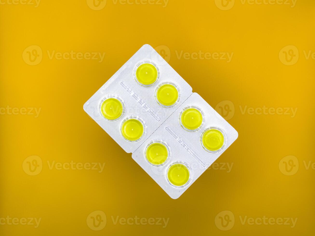 Yellow tablets in silver packaging on yellow background in the center of the image, top view photo