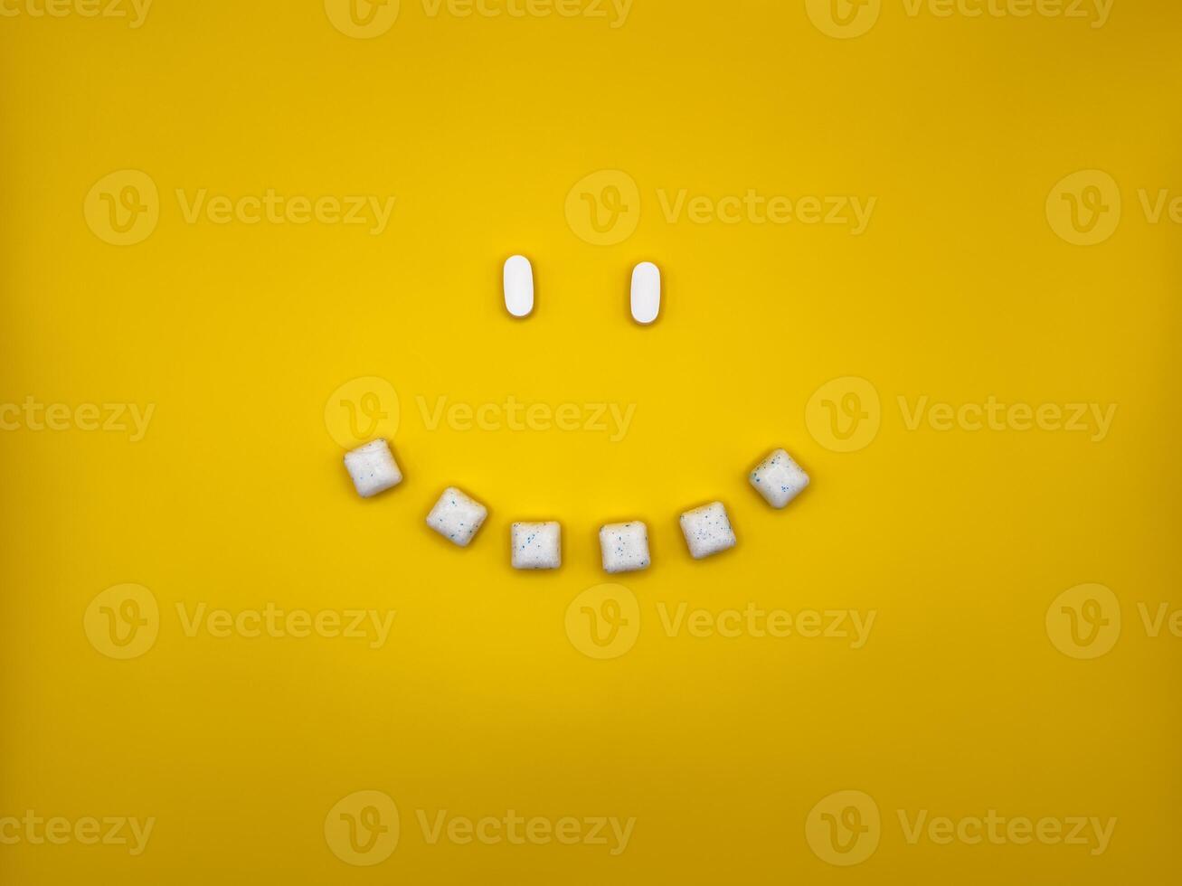 Smiley face with eyes and smile made from chewing gum and pills on yellow background, top view photo