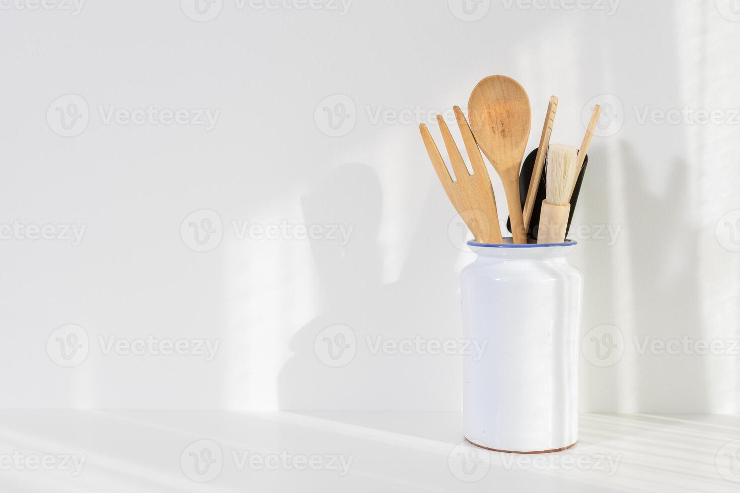 Wooden kitchen utensils in white ceramic container on white background. Cooking background with copy space for menus, recipes photo