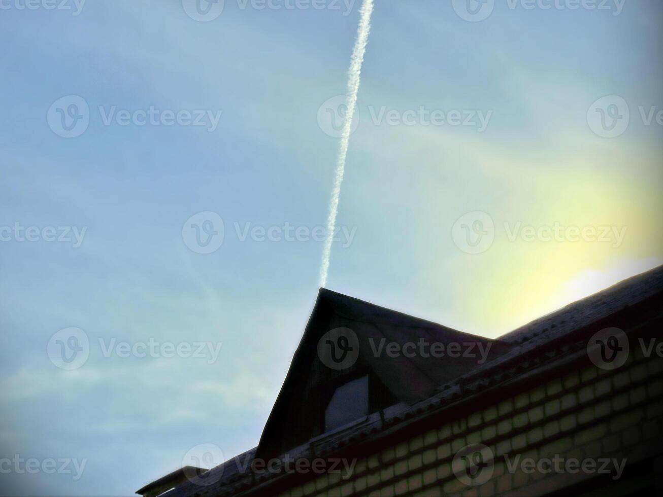 thin plane trail in blue sky above triangular roof, geometric shape in sunlight photo