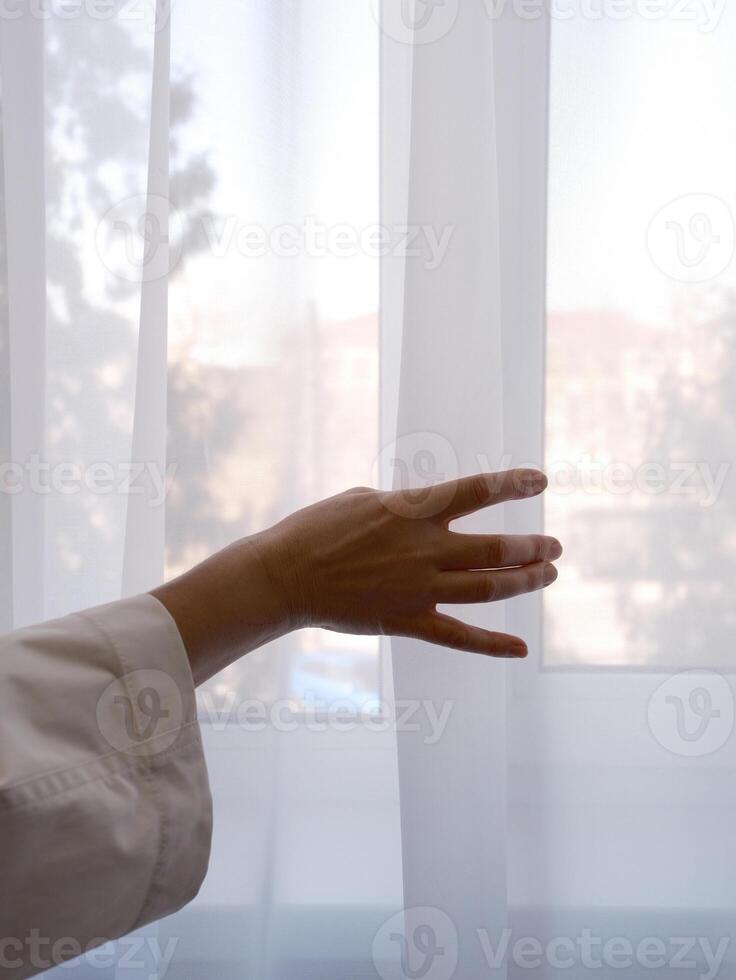 female hand clutching transparent curtain on window photo