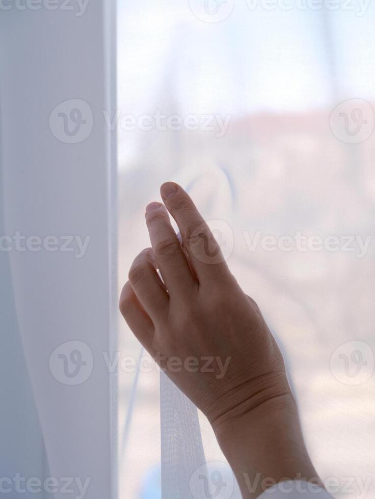 female hand against the background of a window curtained with transparent fabric, copy space photo