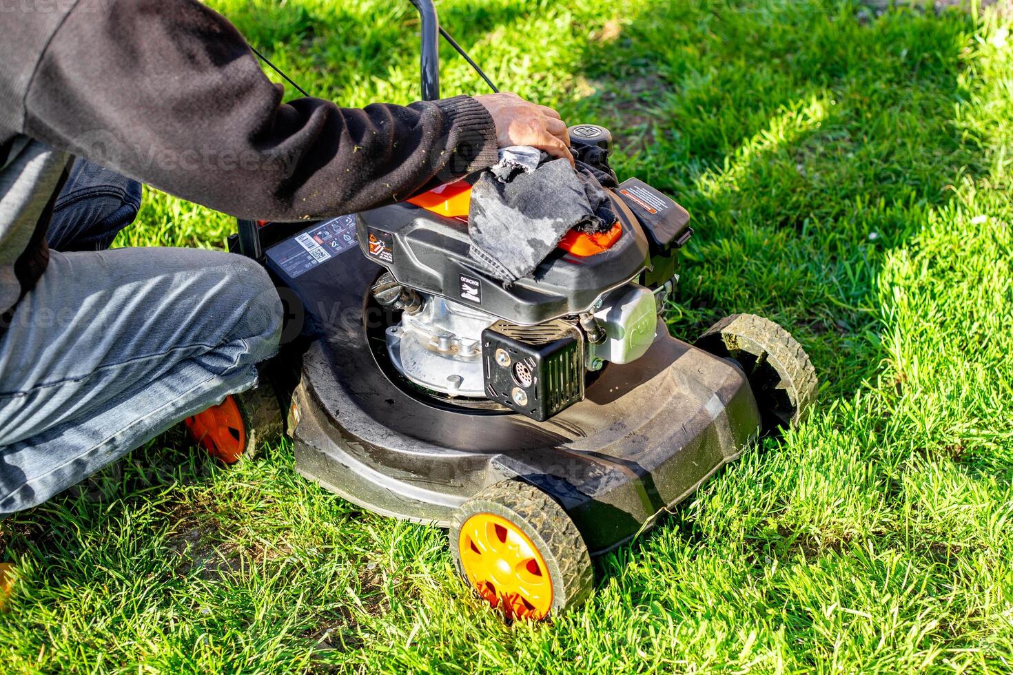 Caring for a petrol lawn mower after mowing the grass. A man wipes the body of the mower with a rag photo
