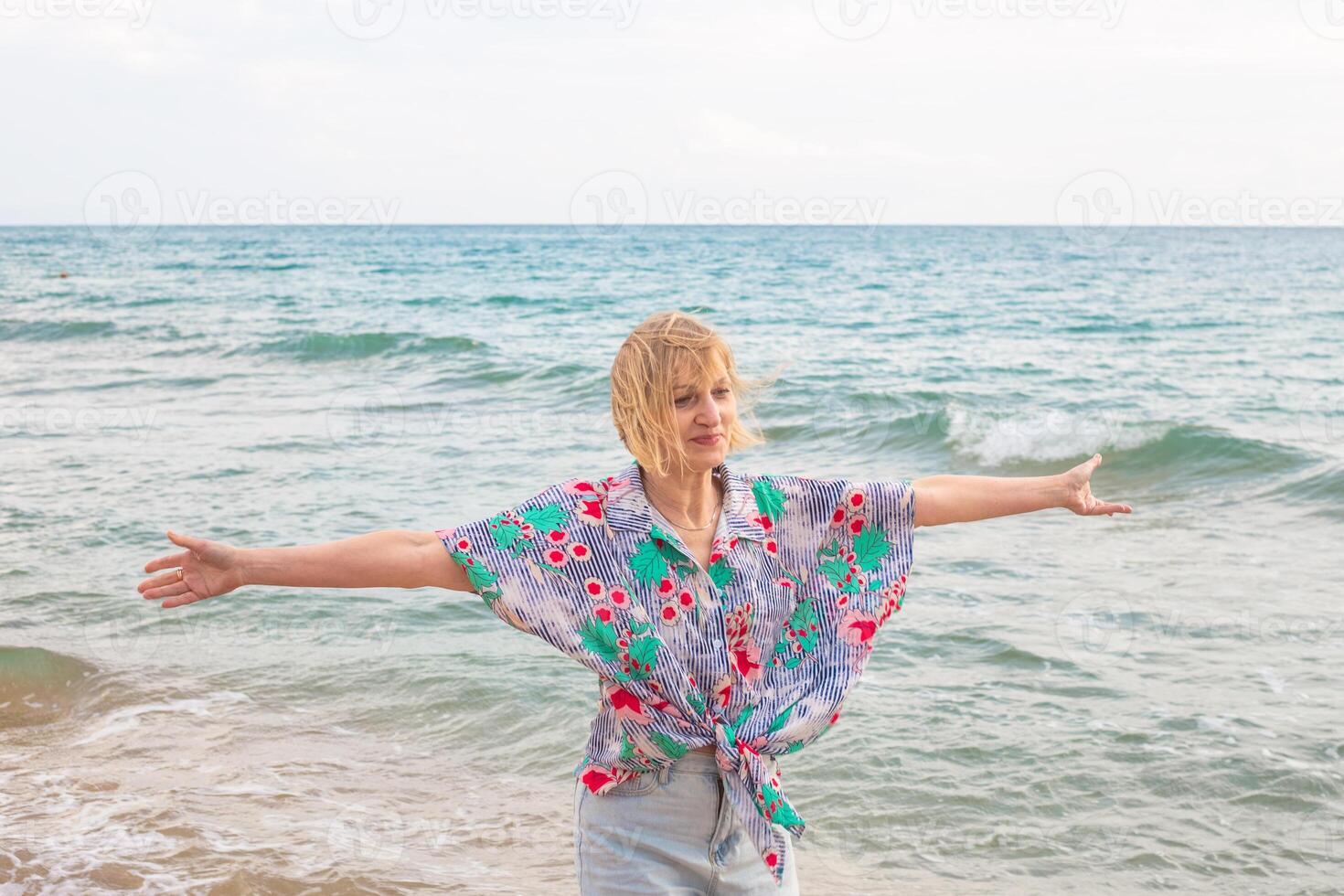 Woman standing on beach with open arms and contented expression. Happy summer vacation at sea photo