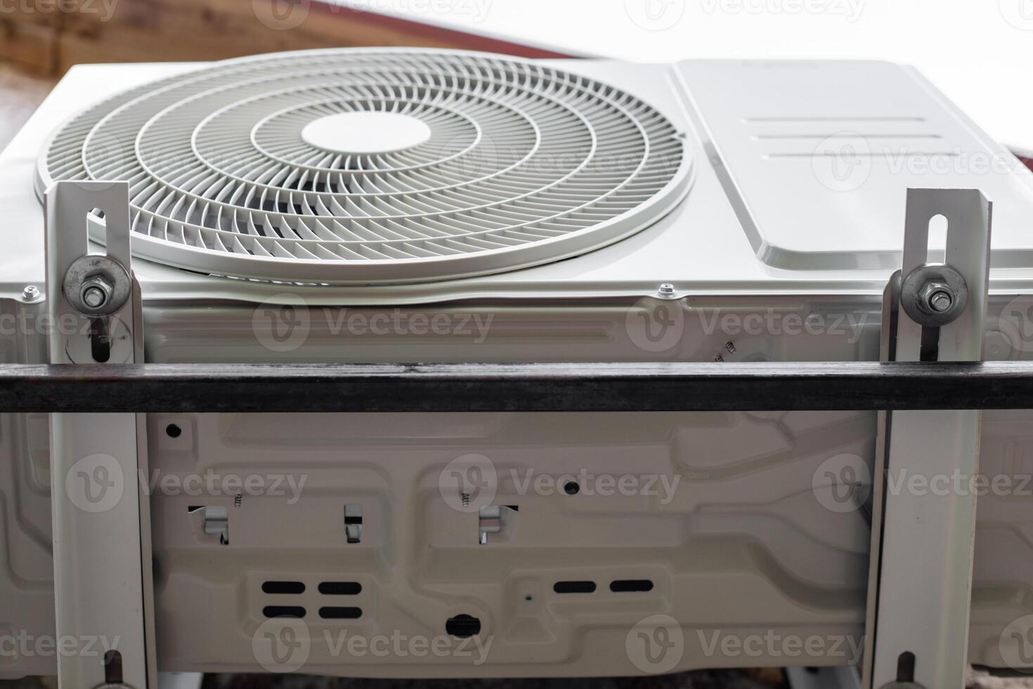 The outdoor unit of the air conditioner is fixed with bolts to brackets on the wall of a rural house photo