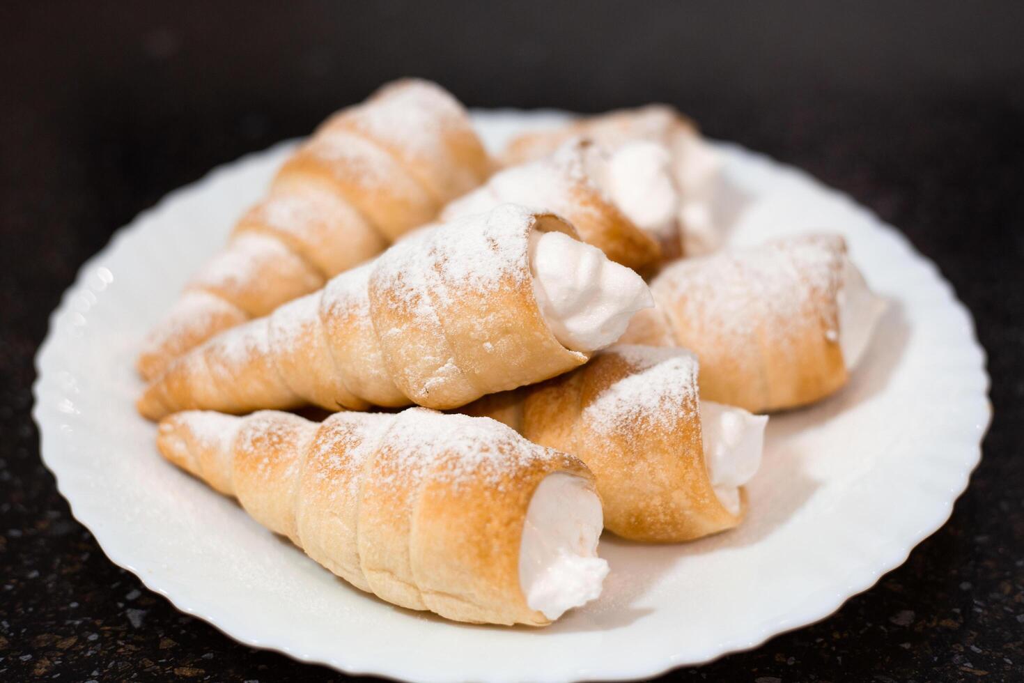 Fragrant puff pastry tubes with whipped cream on a white plate. Cooking sweet pastries, close-up photo