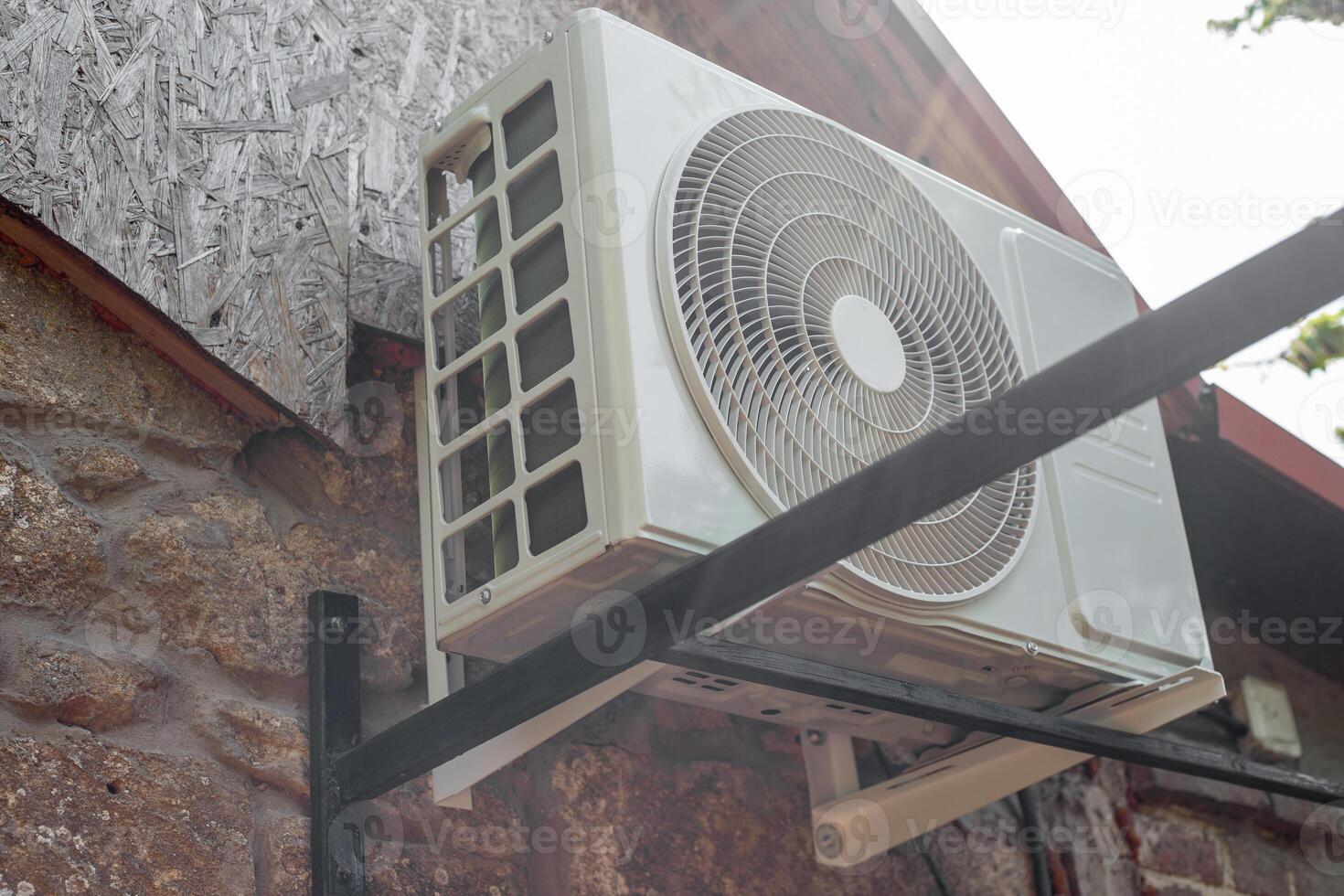 The outdoor unit of the air conditioner is mounted on brackets on the stone wall of a rural house. photo