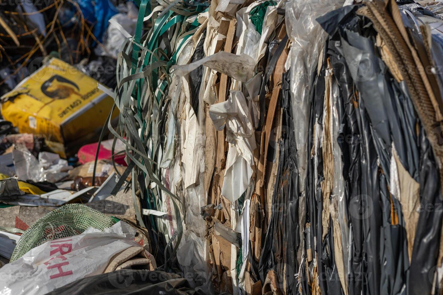 Stacked bales of plastic and cardboard waste are seen in a recycling center, illuminated by midday sunlight, highlighting their textures photo