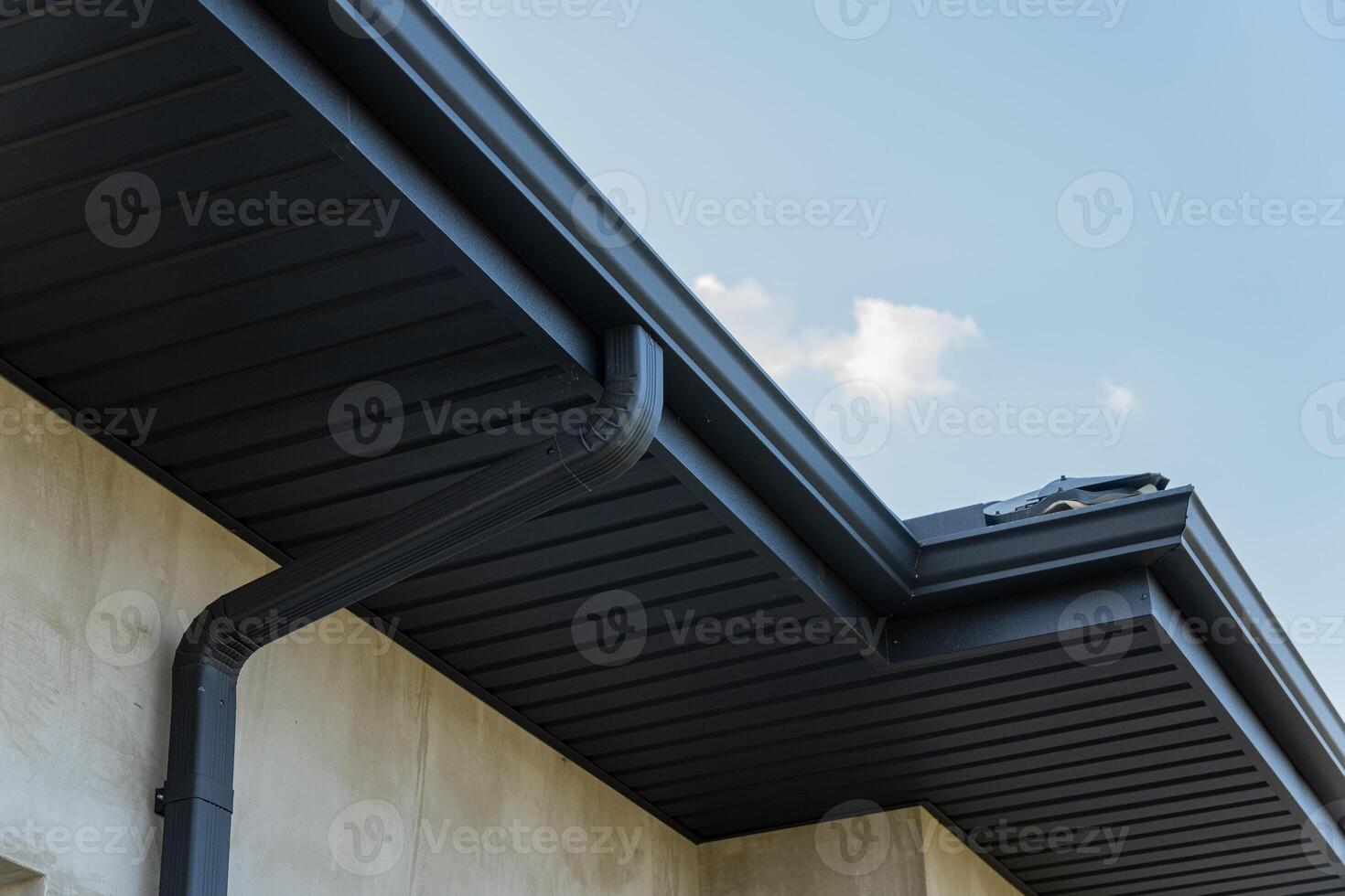 Exterior view of a contemporary home highlighting a sleek black gutter along the roofline under a bright blue sky photo