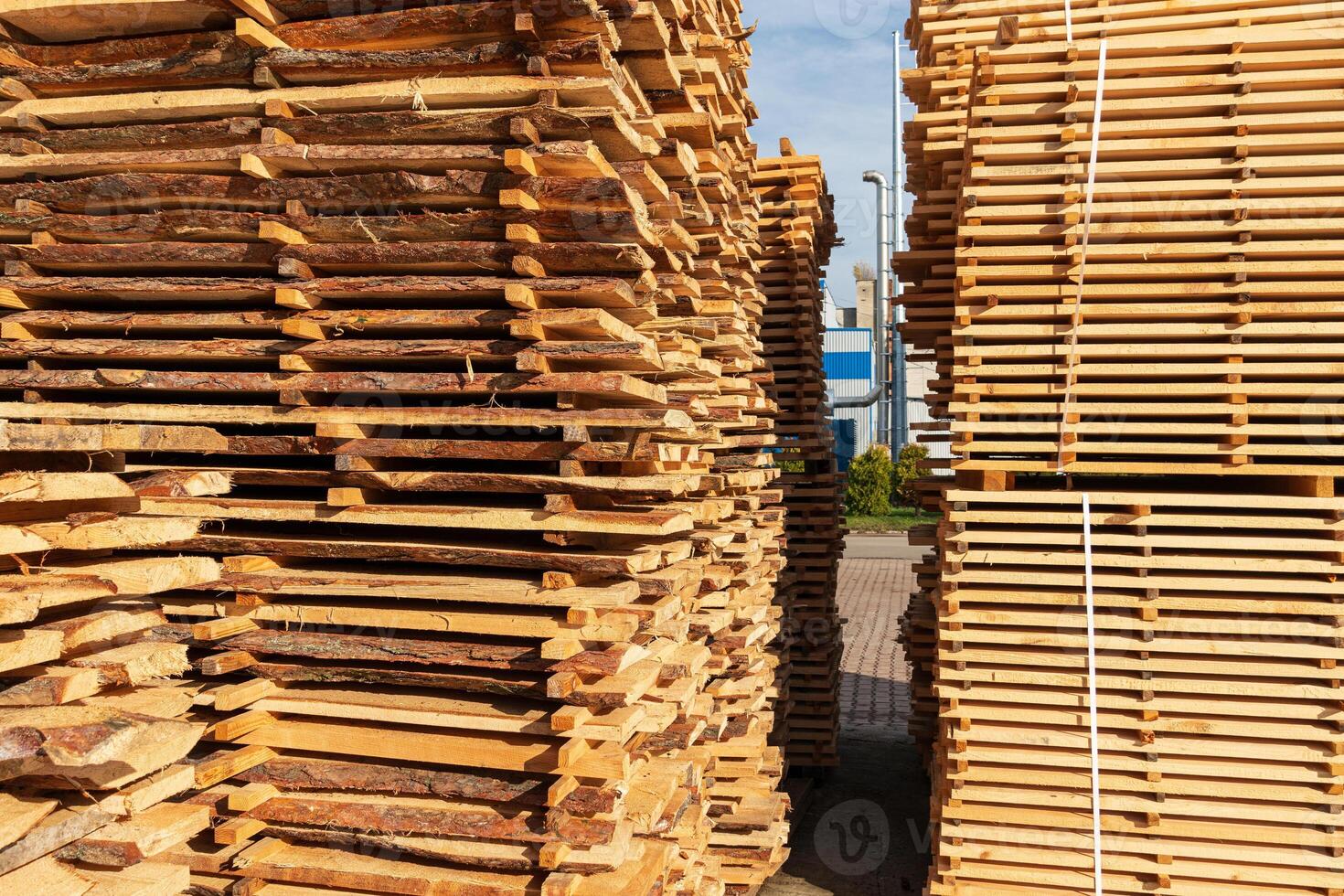 Wooden planks are neatly stacked in a lumber yard, showcasing their texture and color under bright sunlight during a clear day photo