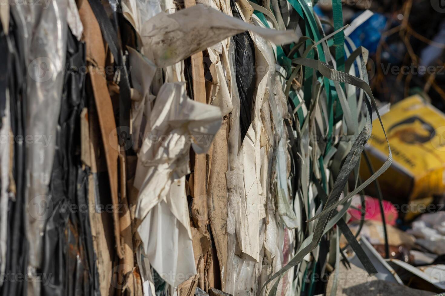 A close-up view reveals a mix of plastic and paper materials stacked together at a recycling center in an urban location under bright sunlight photo