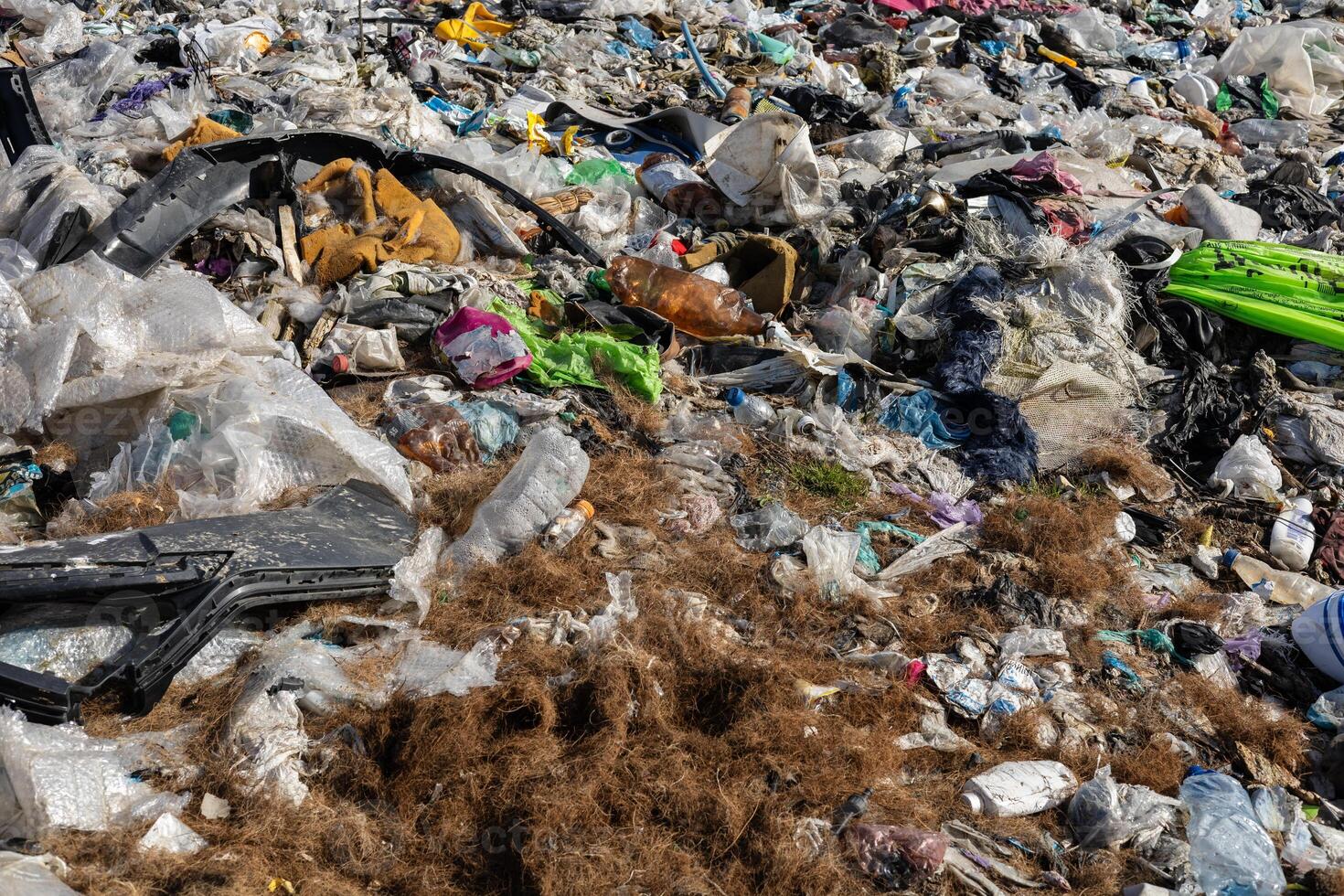 A large area of a landfill site covered with various types of waste such as plastic, fabric, and organic materials during daylight hours photo