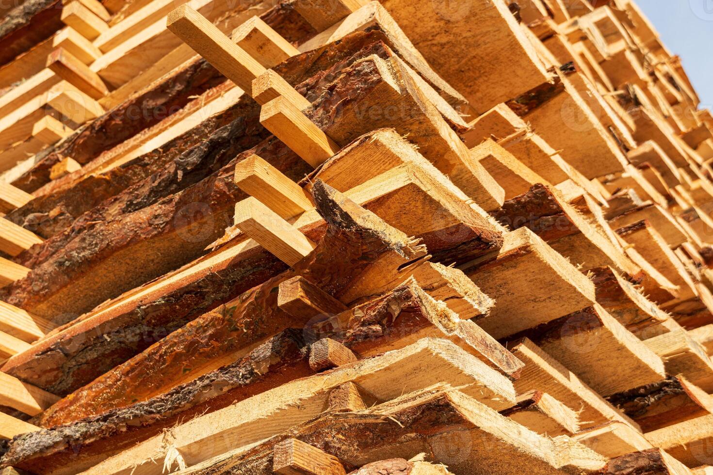 Wooden planks are neatly stacked and drying under the bright sunlight at a lumber yard in the afternoon, showcasing their natural texture photo