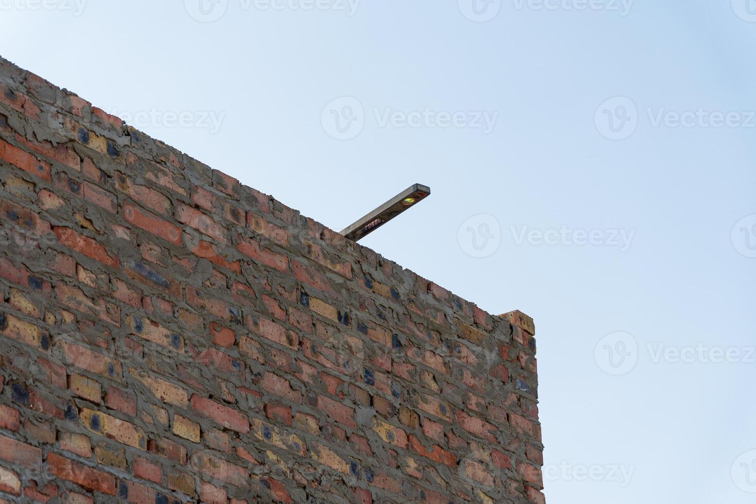 A brick wall stands tall at a construction site, with a level tool resting on the edge under a clear blue sky during daytime photo