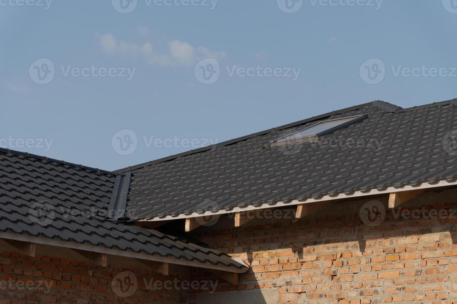 A newly constructed house roof features black tiled shingles and a skylight, set against a clear afternoon sky providing ample light photo