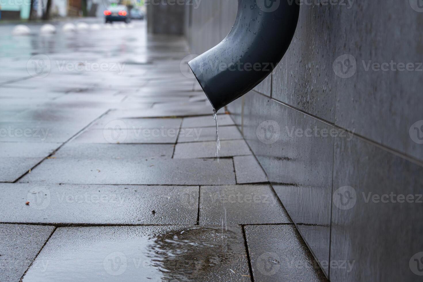 Water drips from a drain pipe onto slick pavement, showing the aftermath of rain in an urban environment photo