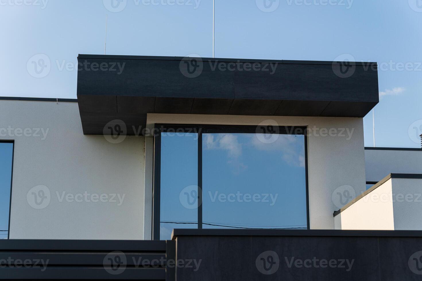 A contemporary building showcases minimalist architecture with a bold overhang and expansive glass panels reflecting the blue sky photo