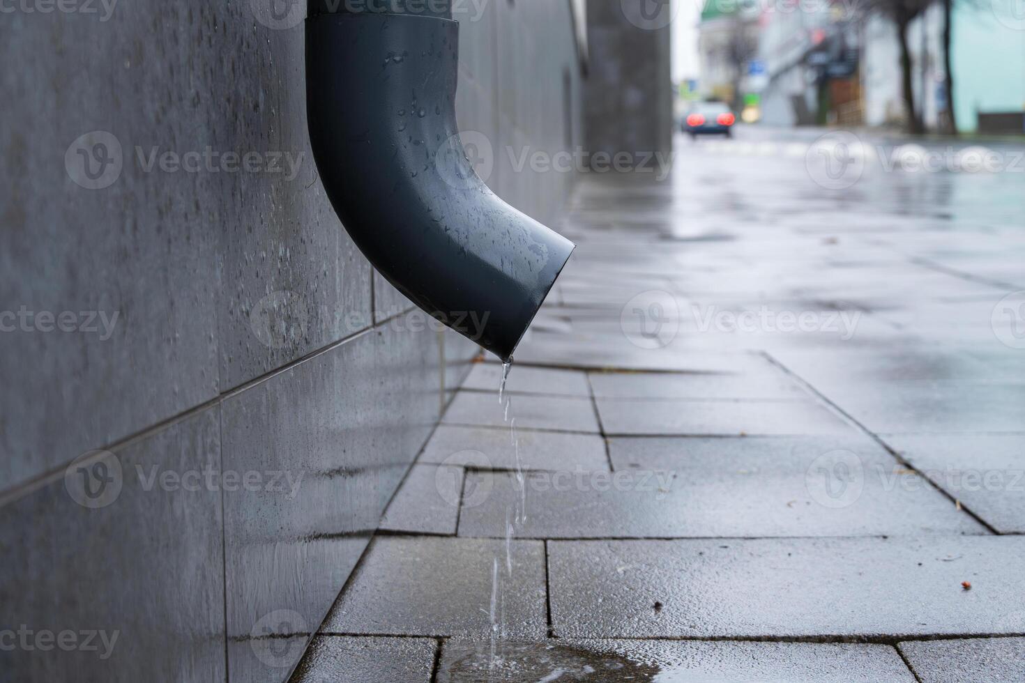 Water continuously drips from a downspout onto the pavement creating small puddles in a city after rain photo