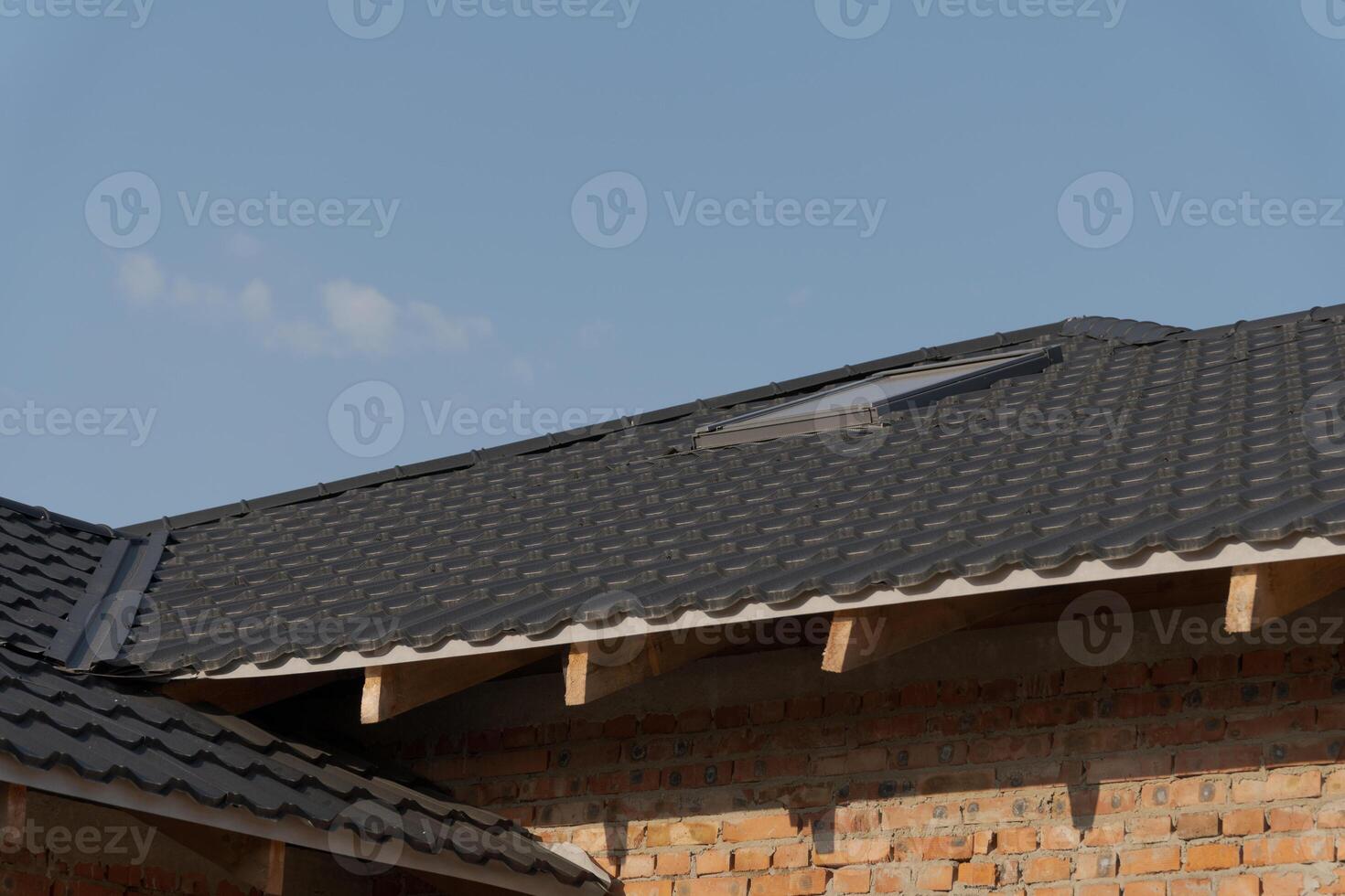 Roof with dark tiles features a skylight, surrounded by brick walls under a clear blue sky, showcasing a modern architectural style photo
