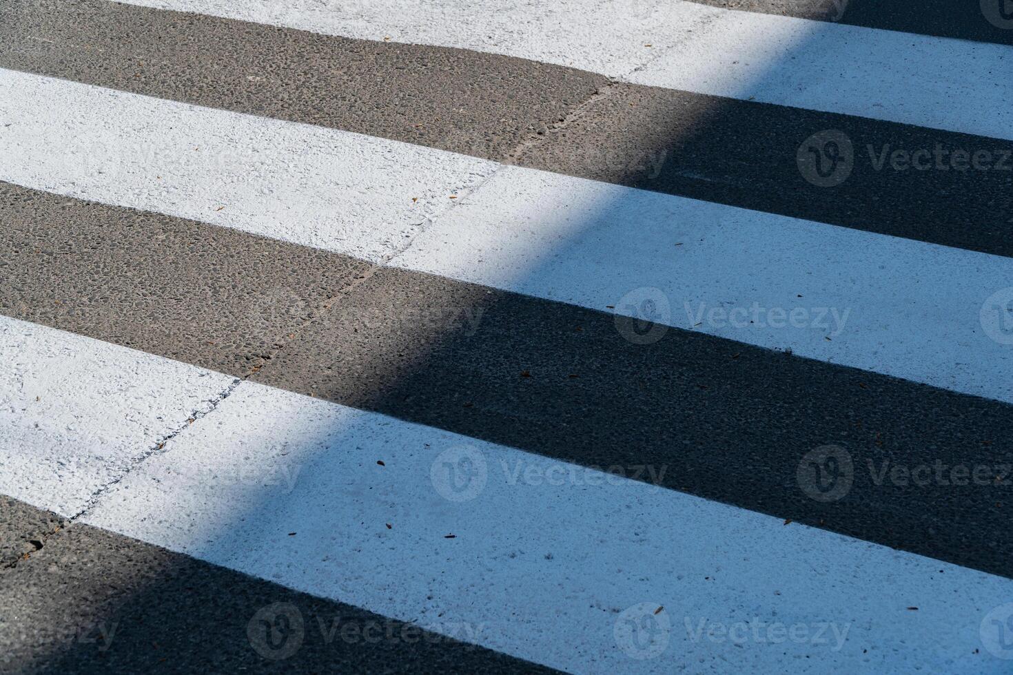 A crosswalk with bold white stripes creates a striking visual against the asphalt, accentuated by a shadow in the afternoon light photo