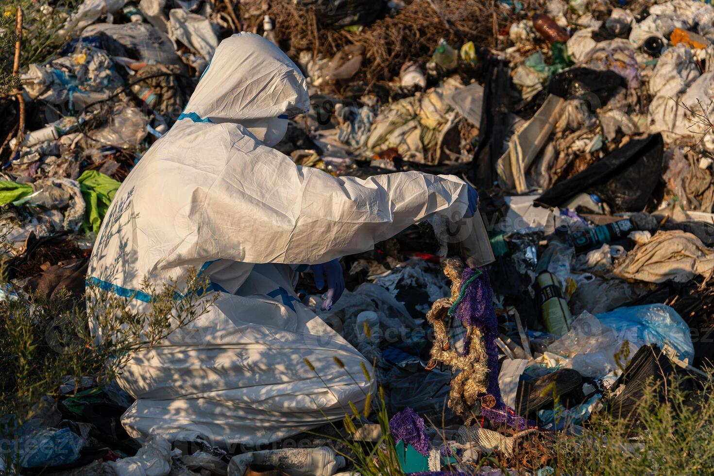 An environmental worker in protective gear is sorting through trash in a landfill during sunset, aiming to clean up plastic waste photo