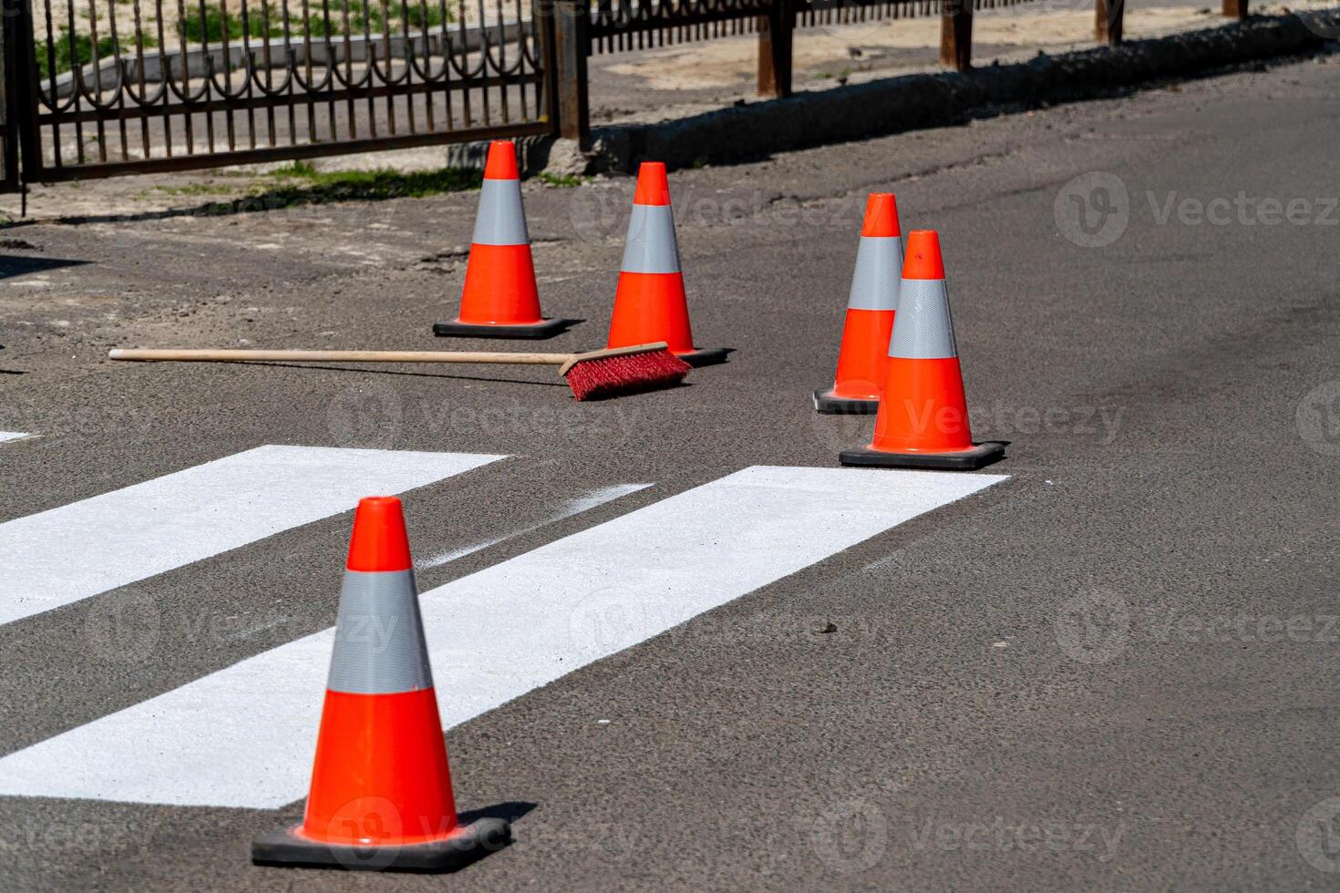 Brightly colored safety cones and a broom lie near freshly painted street lines under clear skies, indicating ongoing road work photo