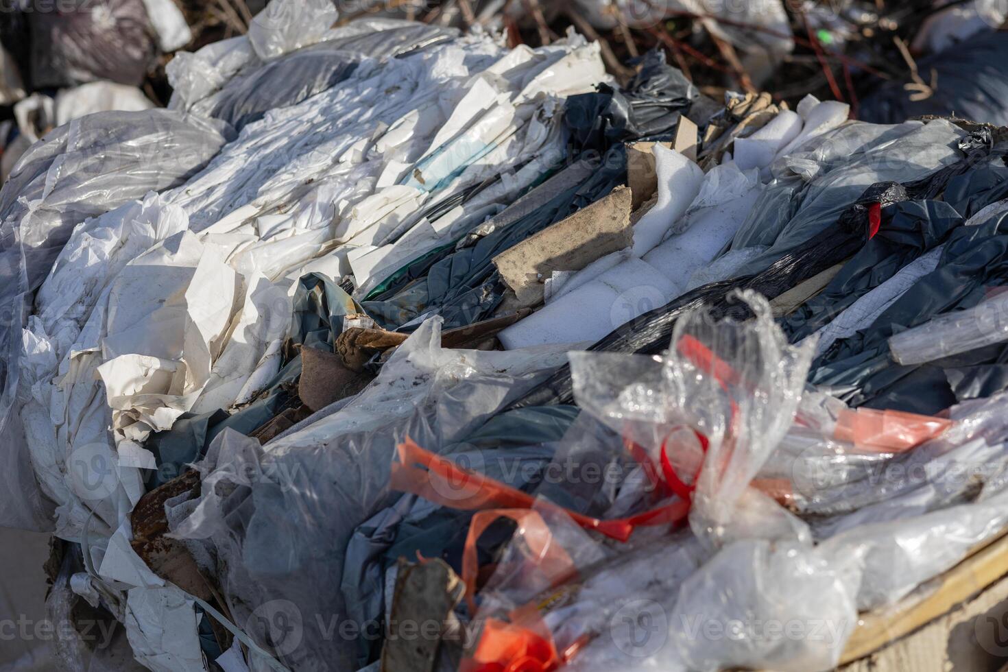 A collection of discarded plastic and paper waste is stacked haphazardly in an industrial setting under clear skies, showcasing recycling issues photo