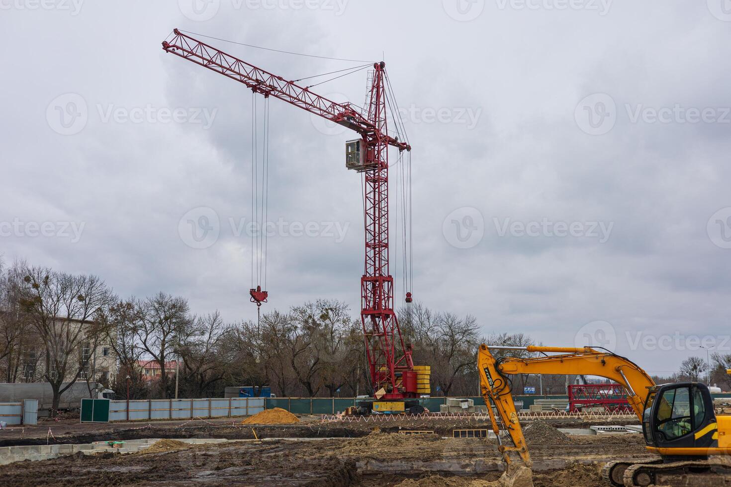 A large red crane stands at a construction site with heavy machinery working amid overcast weather, indicating ongoing building activity photo
