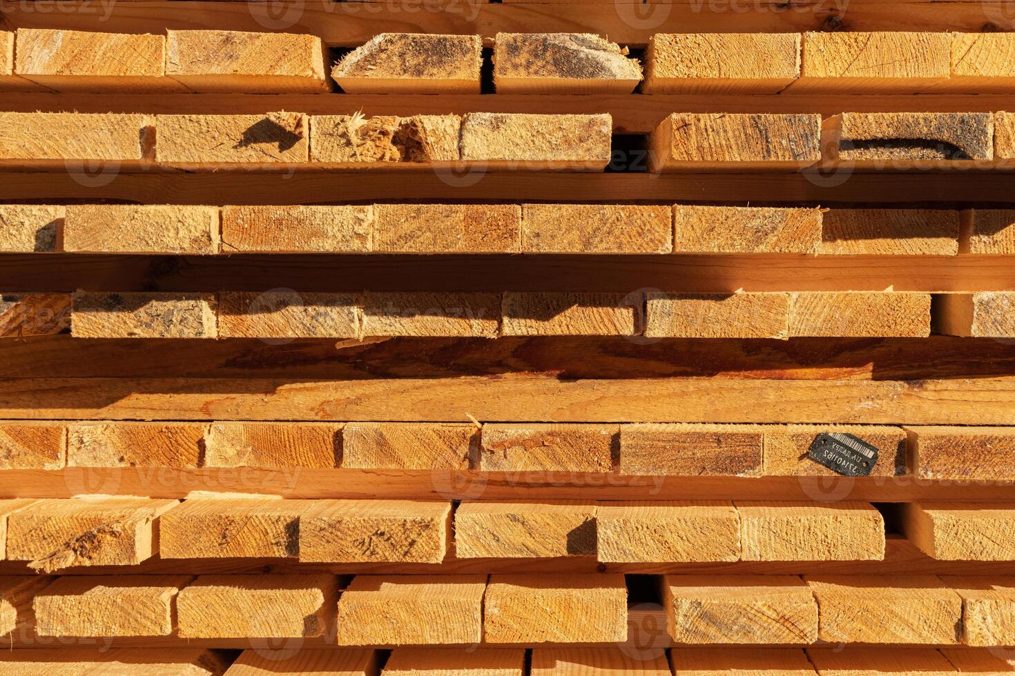Wooden planks stacked in an orderly manner at a lumber yard, showcasing their natural grain and texture illuminated by the afternoon sun photo