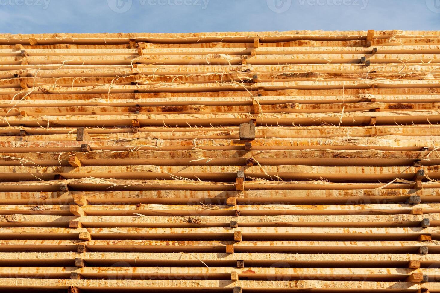 Piles of wooden beams rest against a blue sky, showcasing their natural color and texture in a construction area photo