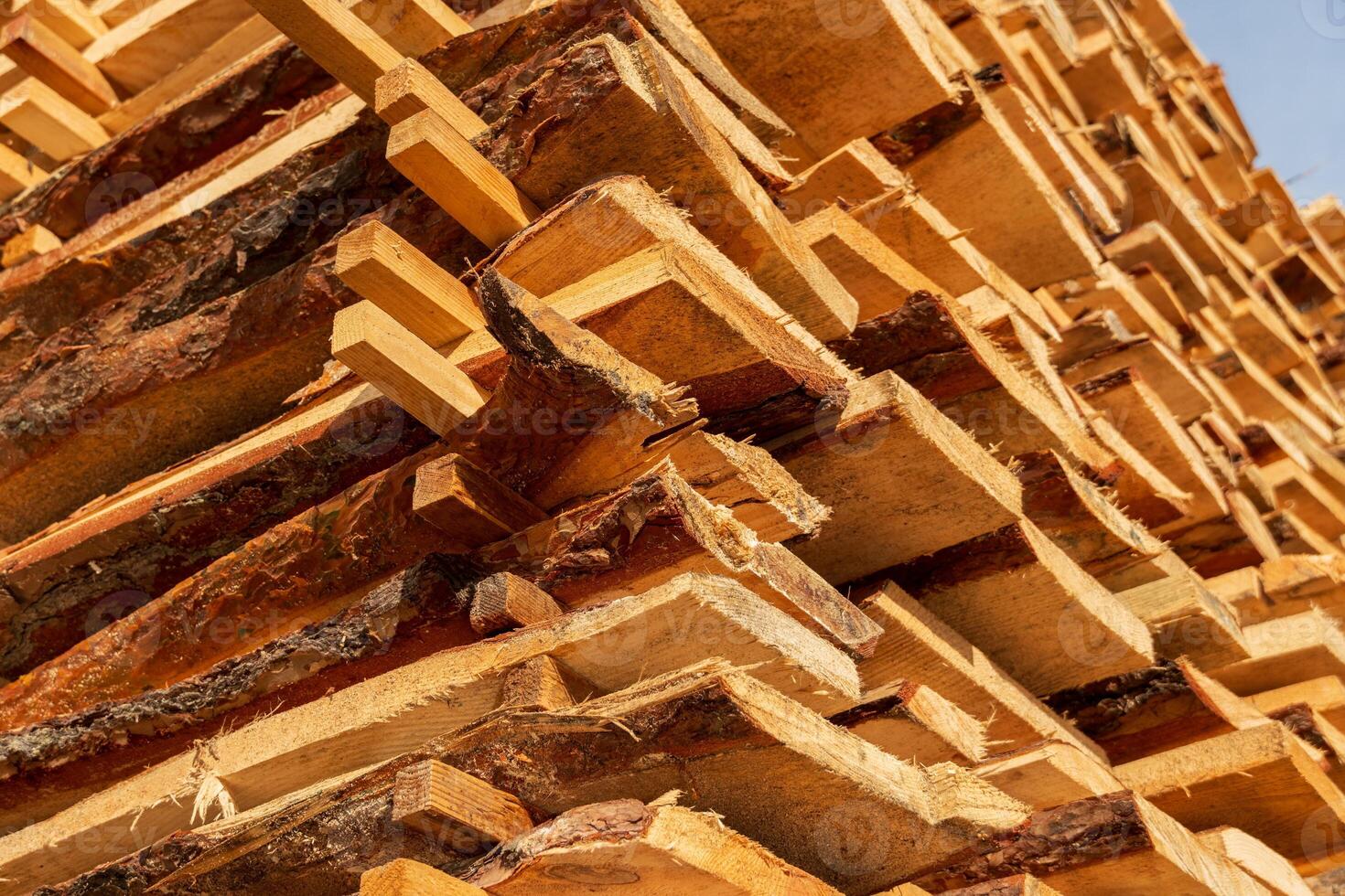 Wooden planks are neatly stacked, showcasing their natural textures and patterns under bright sunlight in a rural lumber yard photo