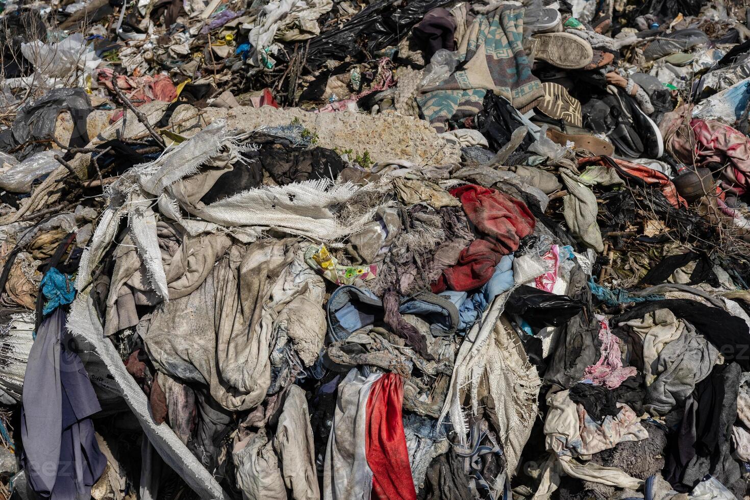 A vast pile of discarded clothes and textiles accumulates at a landfill under bright sun, showcasing the issue of waste management photo