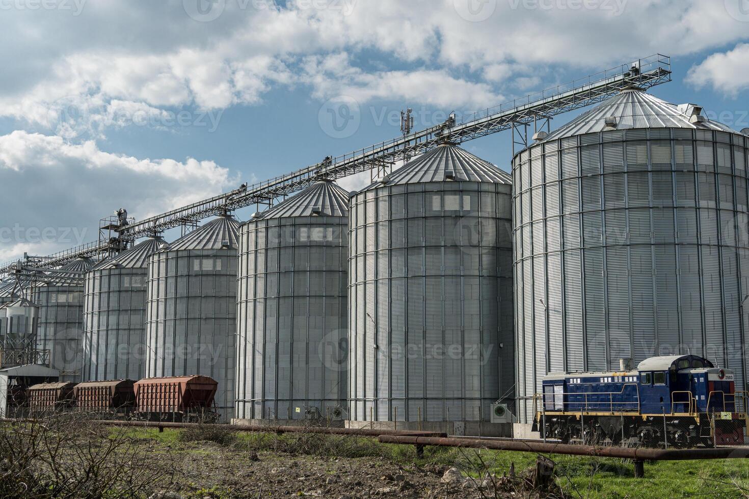 Steel silos used for grain storage stand tall beside a train at an agricultural site under a partly cloudy sky photo