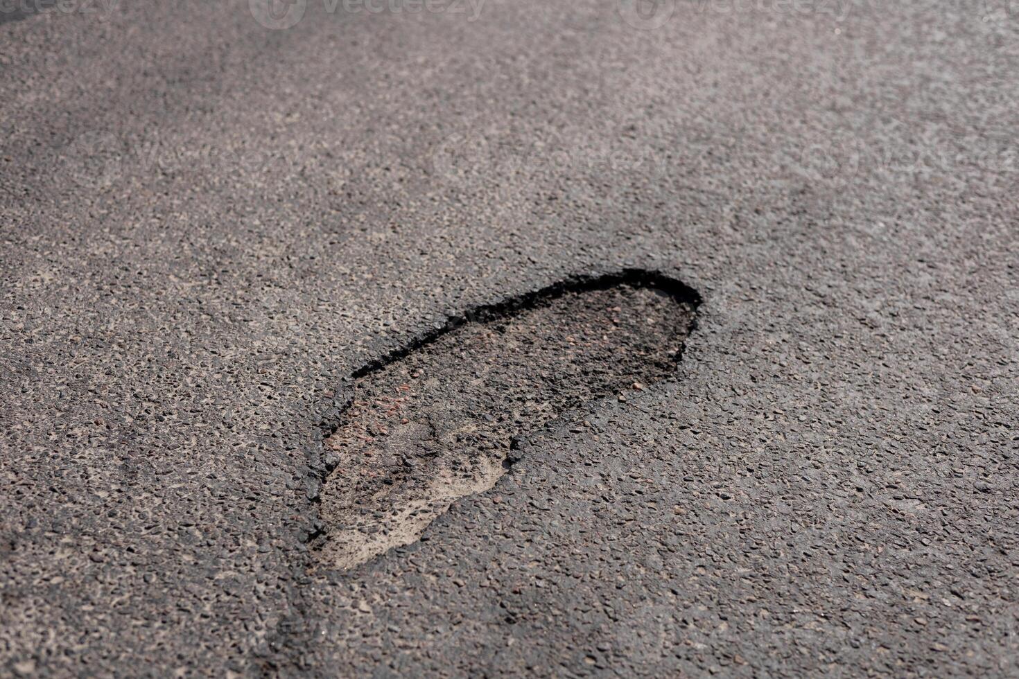 Recent heavy rain has left a substantial footprint-shaped mark in the asphalt of a city street, showing the effects of weather on infrastructure photo