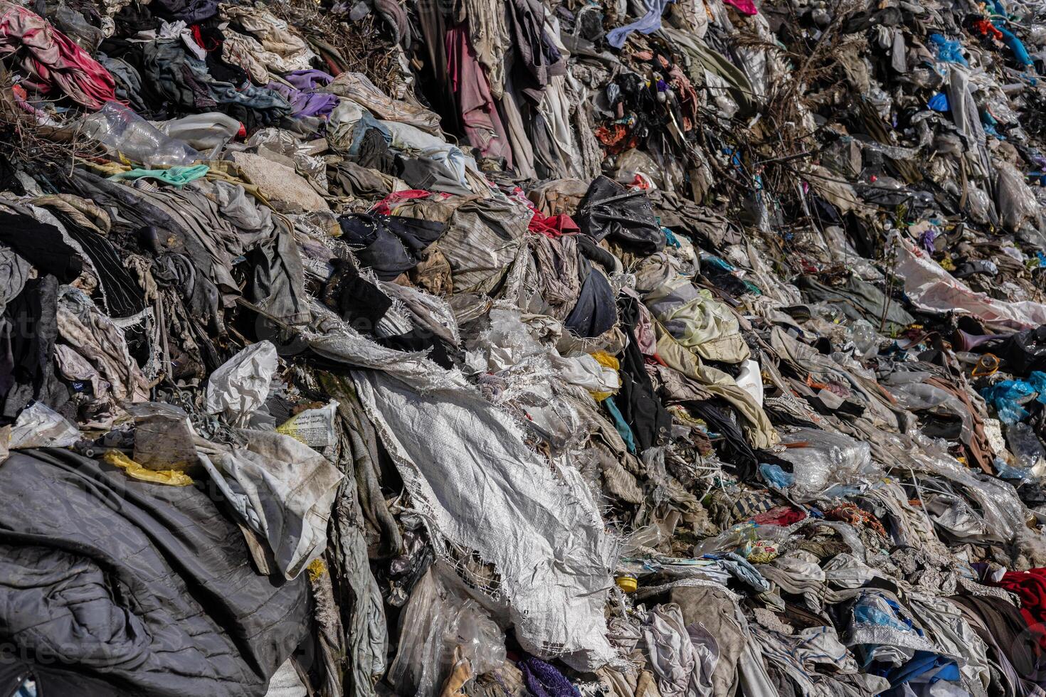 A sprawling landfill showcases a mixture of brightly colored fabrics and plastics piling up, highlighting ongoing pollution issues in the ecosystem photo