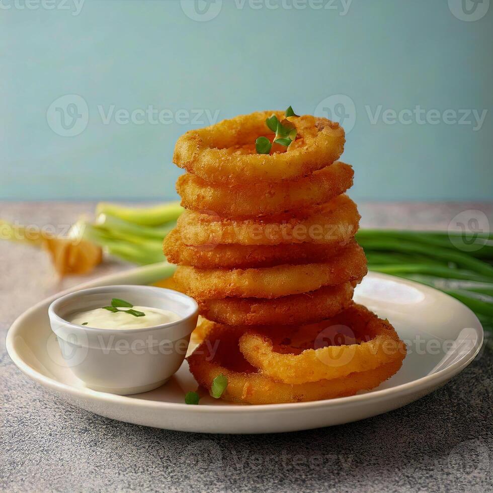A stack of crispy onion rings served with a side of dipping sauce, garnished with chives and fresh herbs on a white plate. photo