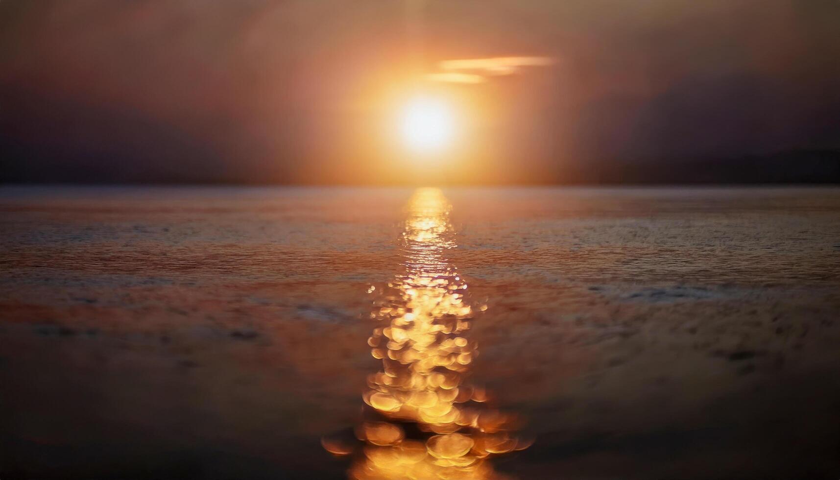 A bright sun emerging above the horizon of a smooth ocean, spreading golden light across the calm waters, evoking warmth and natural energy. photo
