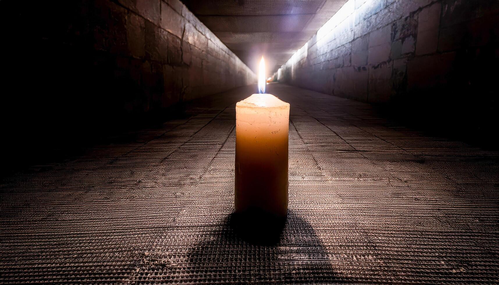 Single candle with a bright flame in the center of a dark, textured tunnel or corridor, casting a long shadow. Evokes a sense of hope and guidance in a mysterious place. photo