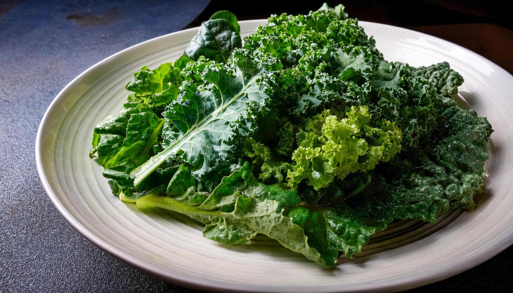 A white plate filled with a variety of fresh, vibrant green kale leaves, including lacinato, curly, and possibly collard greens, showcasing their different textures and shapes. photo
