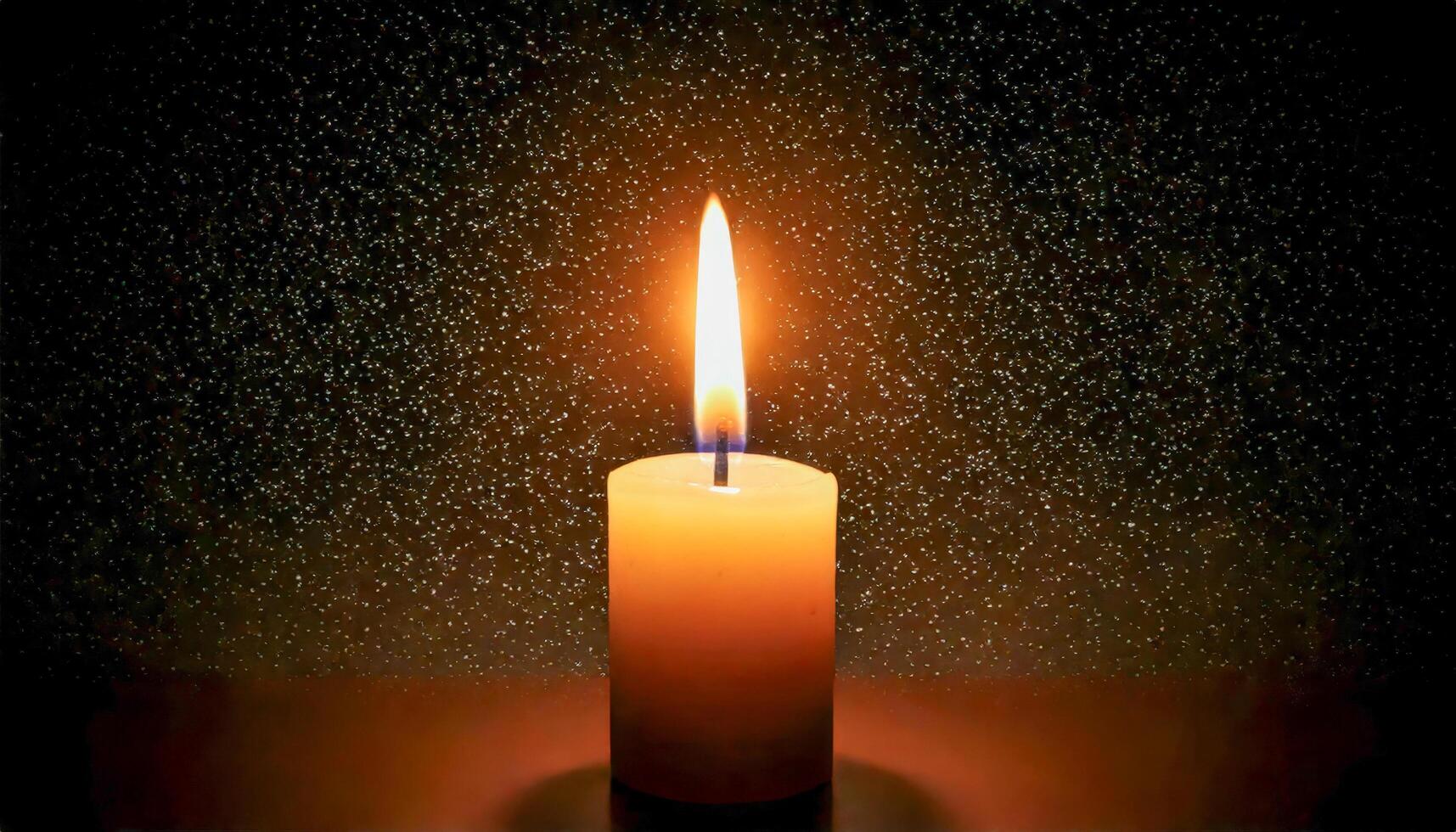 Single candle with a bright flame against a dark, textured background with subtle golden glitter. photo