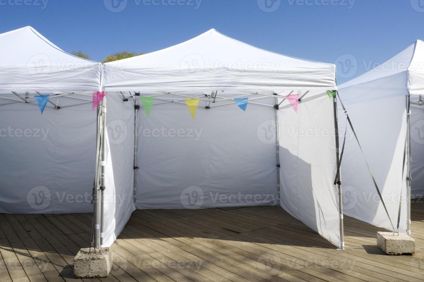White Empty Folding Tents for Commercial Retail Shop with Colorful Bunting Flags on Wooden Deck. Vacant Place is Ready for Local Farmer at City Market, Waiting for New Goods photo