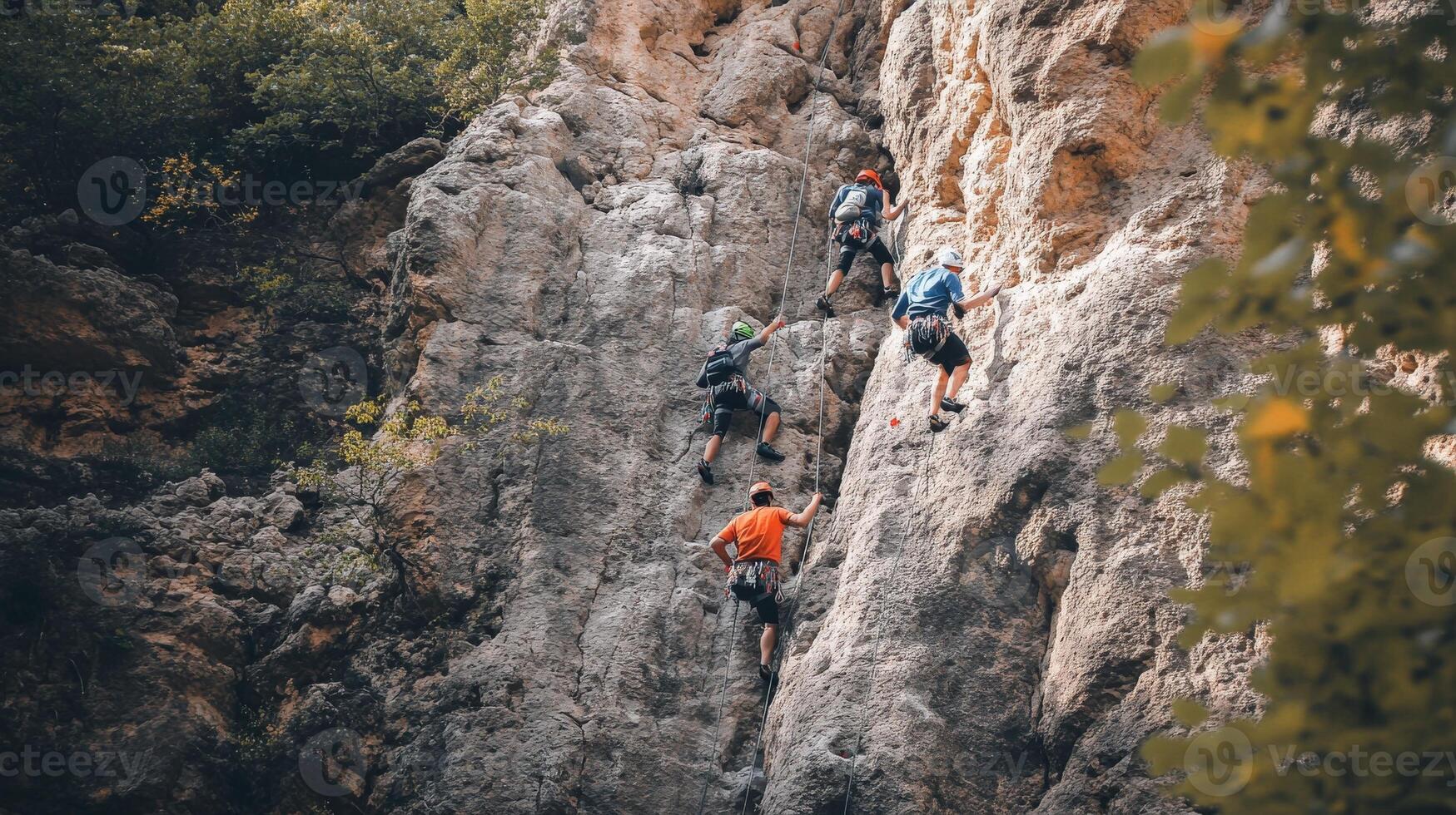 Four rock climbers ascend a steep, gray cliff face. photo