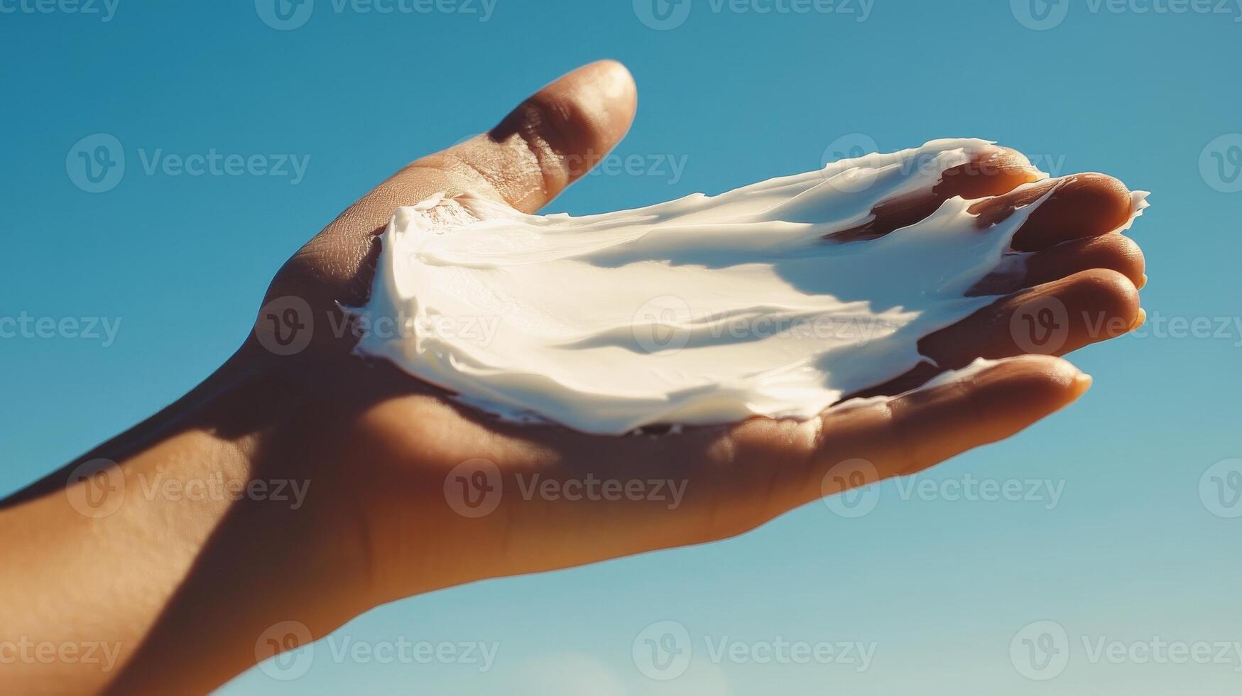 A hand holding a spread of white cosmetic product against a clear sky. photo