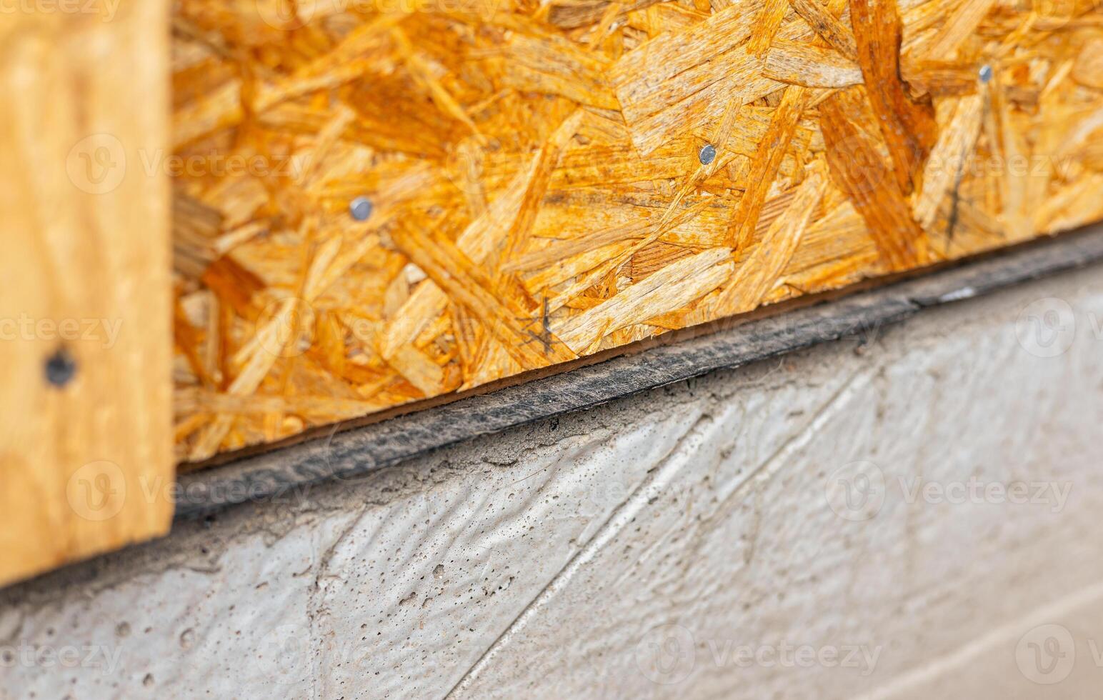 Waterproofing of the house foundation. Close-up of the house foundation with waterproofing. Plywood sheets on a concrete foundation, installation of OSB wall panels. photo