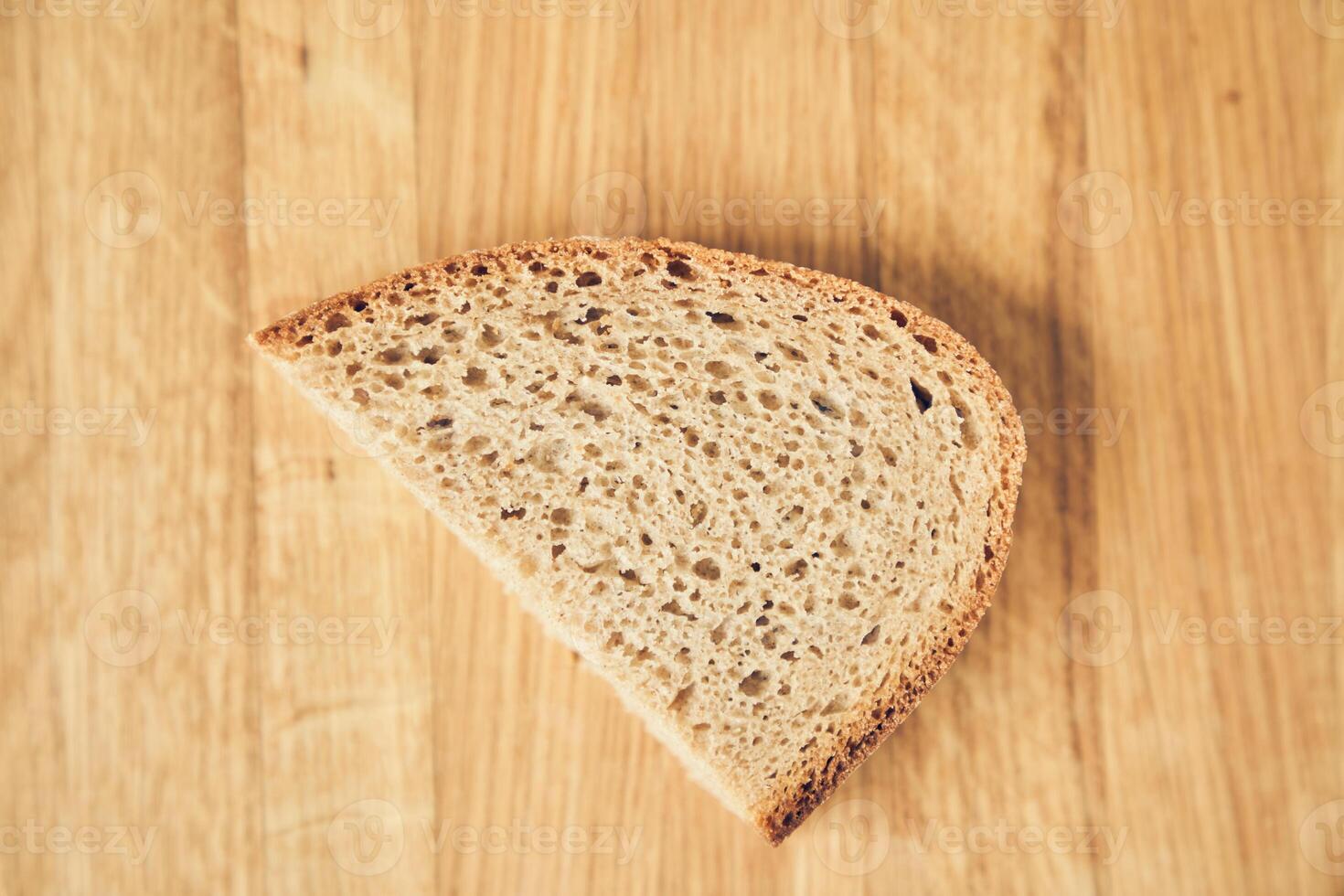 One slice of dark gluten-free rye bread on a wooden board background with space to copy photo