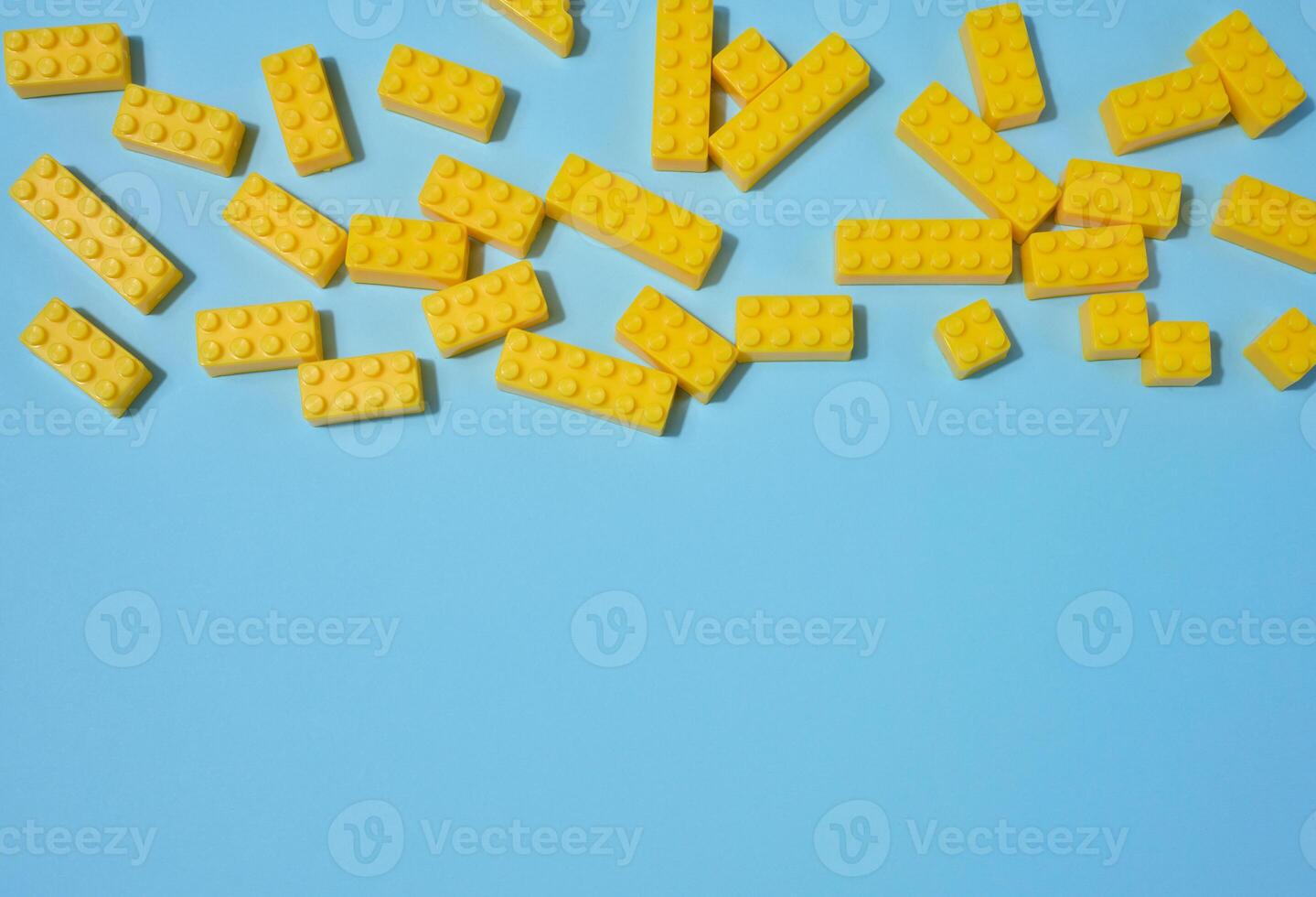 Scattered blue plastic toy building bricks on a solid yellow background. Play, construction, education or creative concept photo