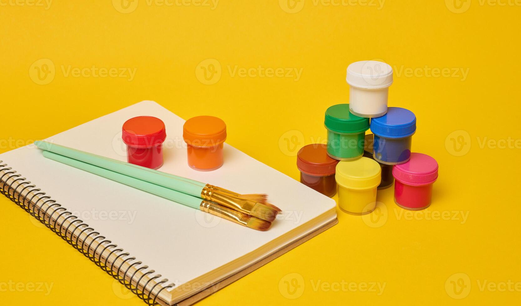 White spiral notebook, brushes and colorful paint cans symbolizing art photo