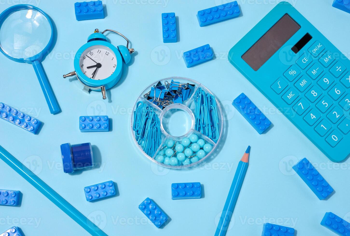 Flat lay of blue stationery, learning items letters, magnifying glass, supplies, and an alarm clock on a blue background. photo