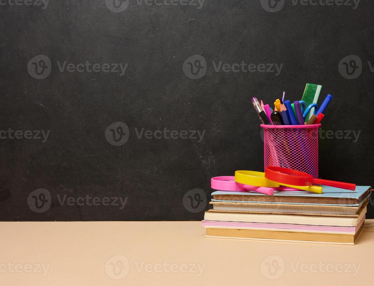 A stack of colorful books, a pink glass with pens and pencils, and two magnifying glasses symbolizing learning, knowledge photo